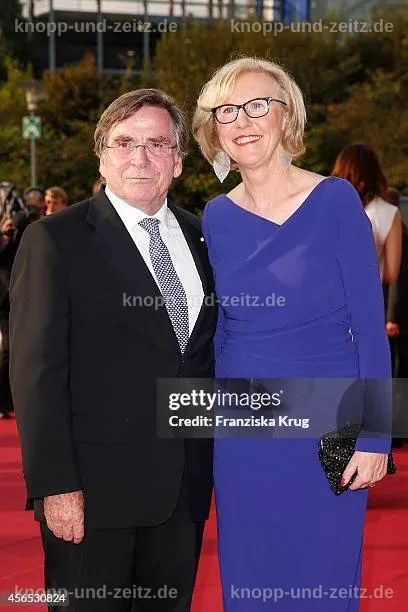 Anita Schlierf posiert in einem stilvollen Outfit vor einer neutralen Kulisse.
